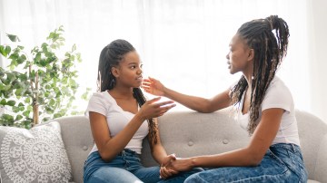A mother and daughter sitting on sofa at home talking