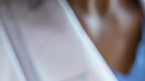 A photo with the focus on the unrecognizable pregnant woman in the foreground as the unrecognizable doctor shows her an ultrasound on a digital tablet in the background.