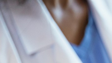 A photo with the focus on the unrecognizable pregnant woman in the foreground as the unrecognizable doctor shows her an ultrasound on a digital tablet in the background.