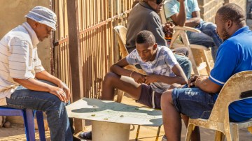 Three african men playing a board game and others drinking in Alexandra Township, Johannesburg. Also known as Alex developed since 1912 and allocated for blacks in the apartheid era, the self governing Alexandra action committee took charge of running Alexandra and now forms part of Johannesburg.