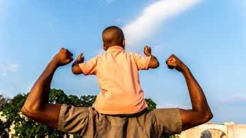 Rear view of a father with his son flexing muscles outdoors