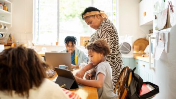 Children sitting at dining table while their mother helping them with homework at home
