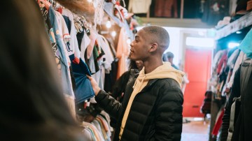 A smiling group of young adults have fun shopping for retro and vintage clothing styles at a second hand thrift store. Mixed ethnic group. Horizontal image with copy space.