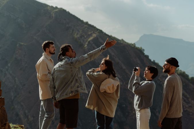 A group of five people standing on a mountain overlook, with one person gesturing while others are attentively watching and taking photos.