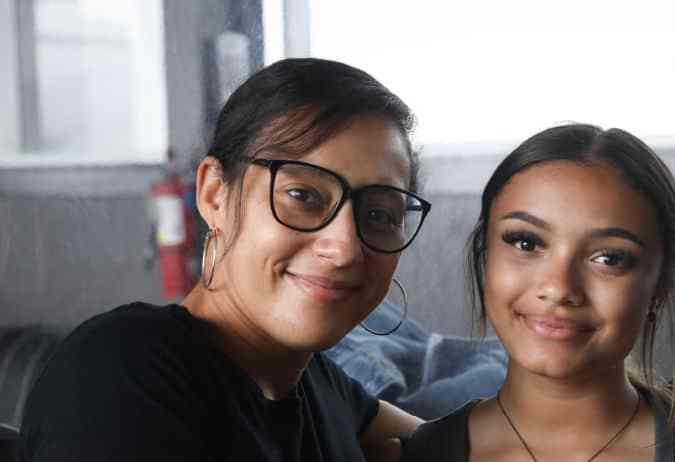 A young woman sits between two smiling adults, all wearing black shirts. They are posing together with friendly expressions in a casual indoor setting.
