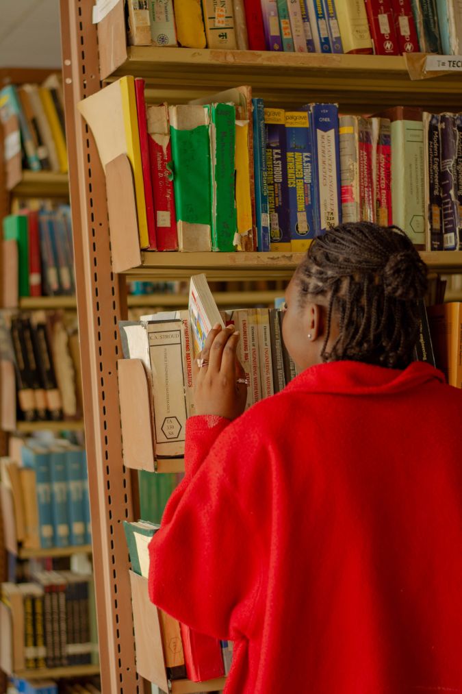 A person wearing a red sweater reaches for a book on a shelf in a library filled with colorful books.